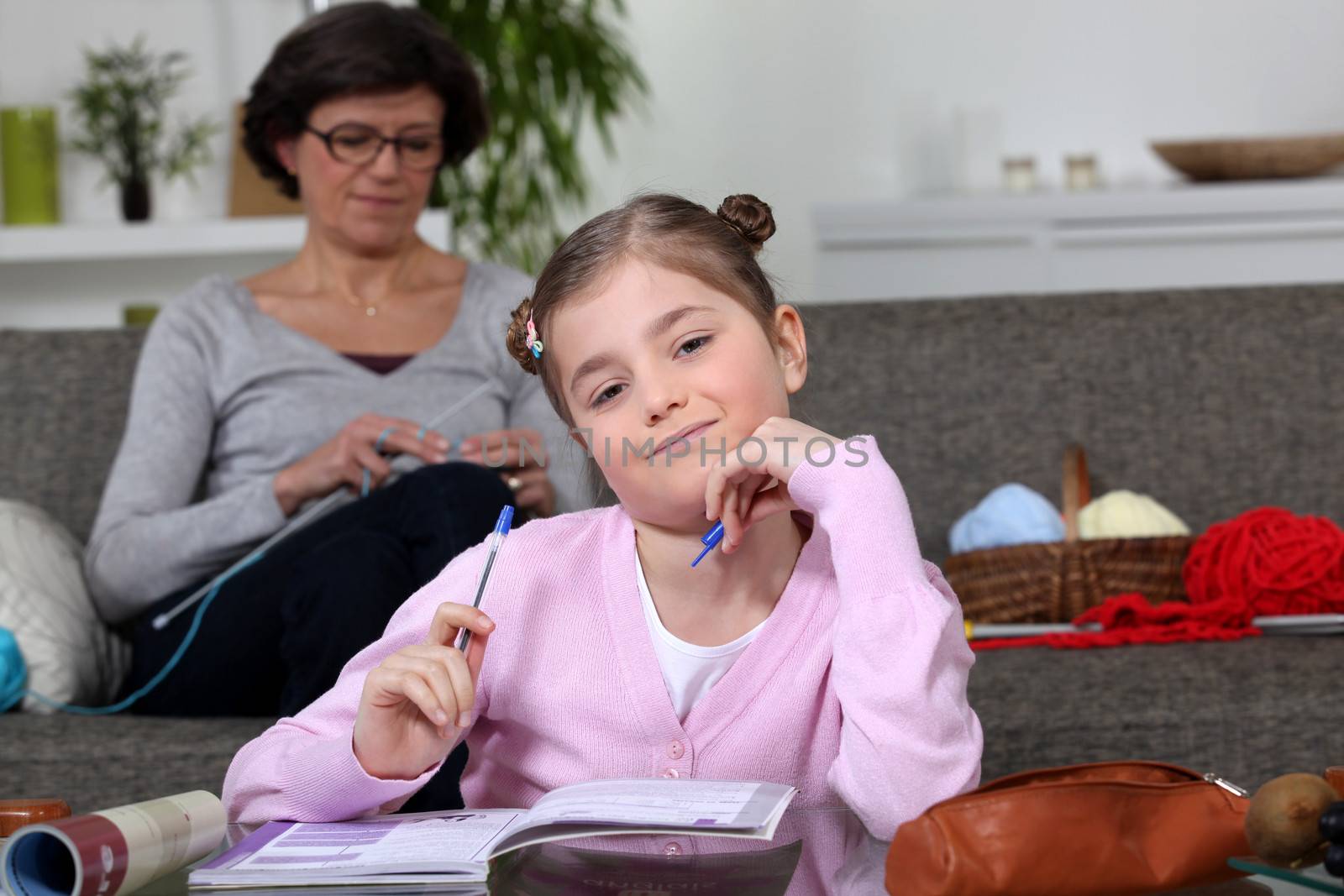 Little girl doing her homework whilst her mom is sewing by phovoir
