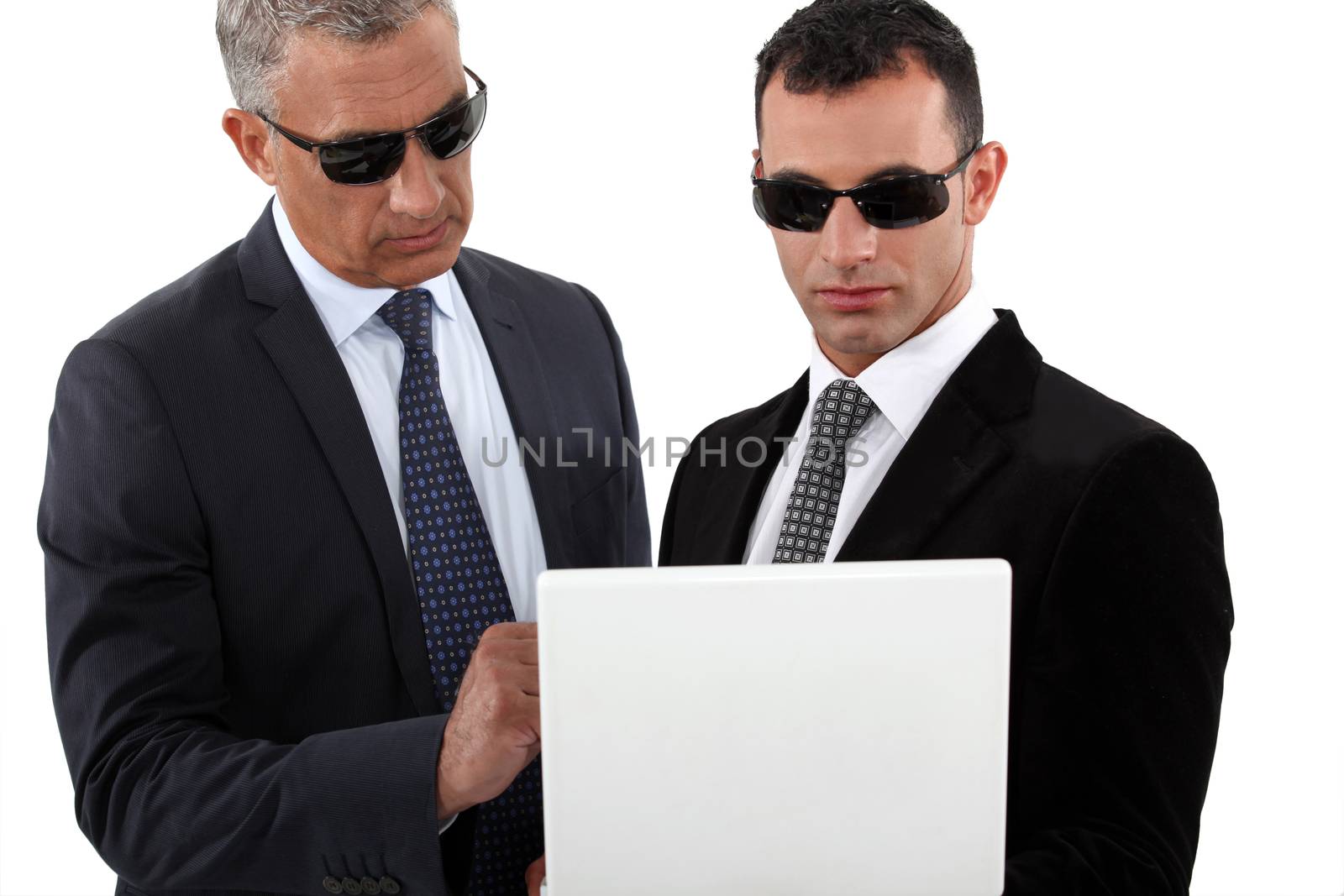 Serious men in smart suits with sunglasses holding a laptop by phovoir