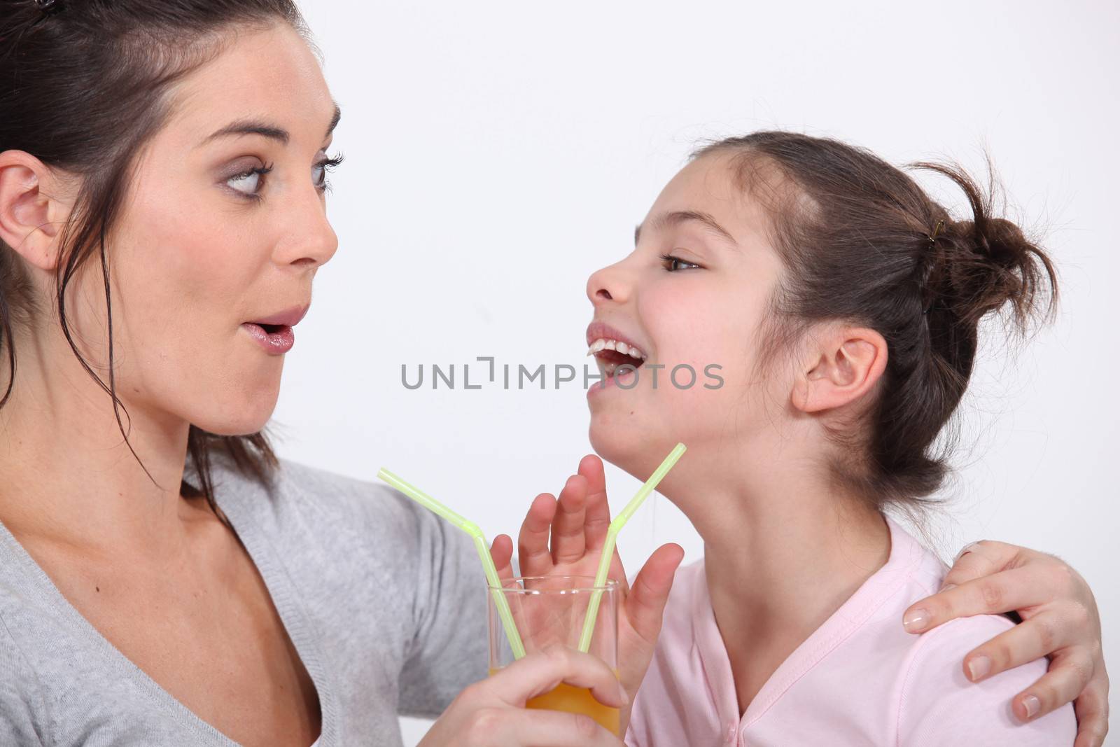 Mother and daughter drinking from the same glass by phovoir