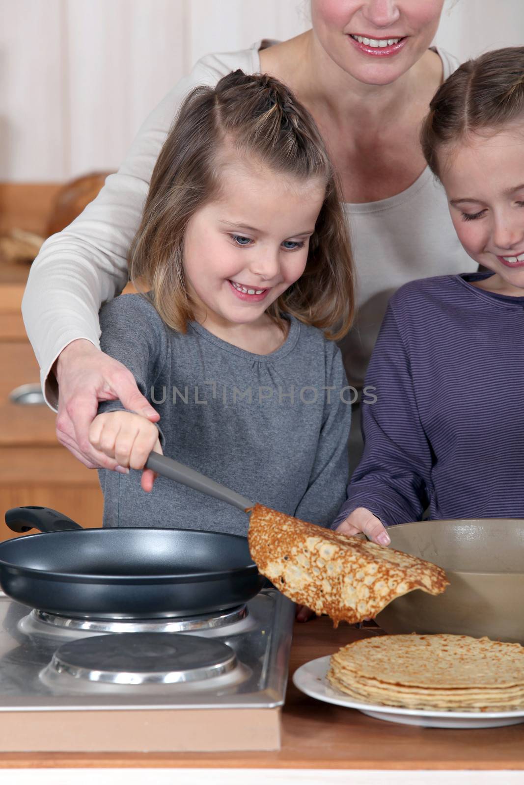 Mother making pancakes with her two daughters by phovoir