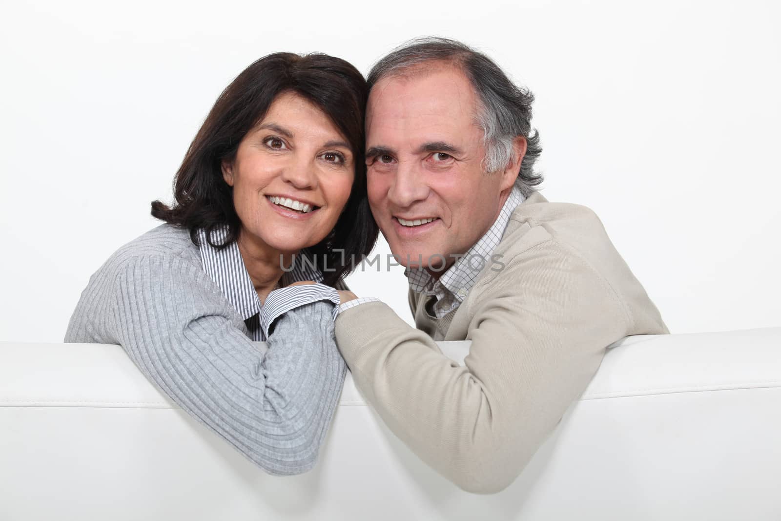 happy mature couple sitting on the couch by phovoir