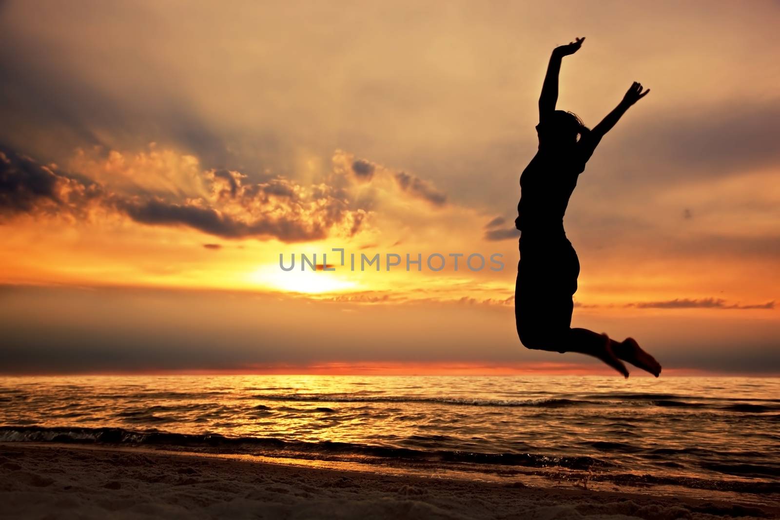 Happy woman jumping on the beach at sunset by photocreo