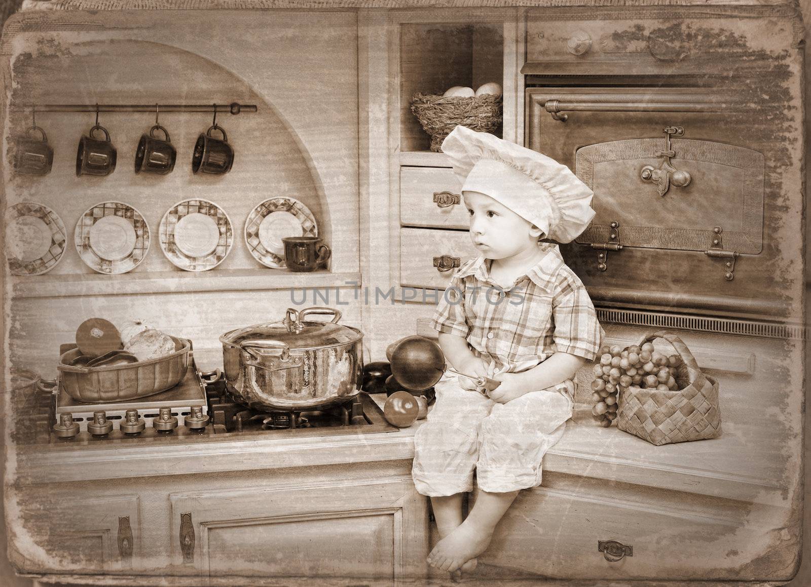 little boy sits on a kitchen table and plays the cook