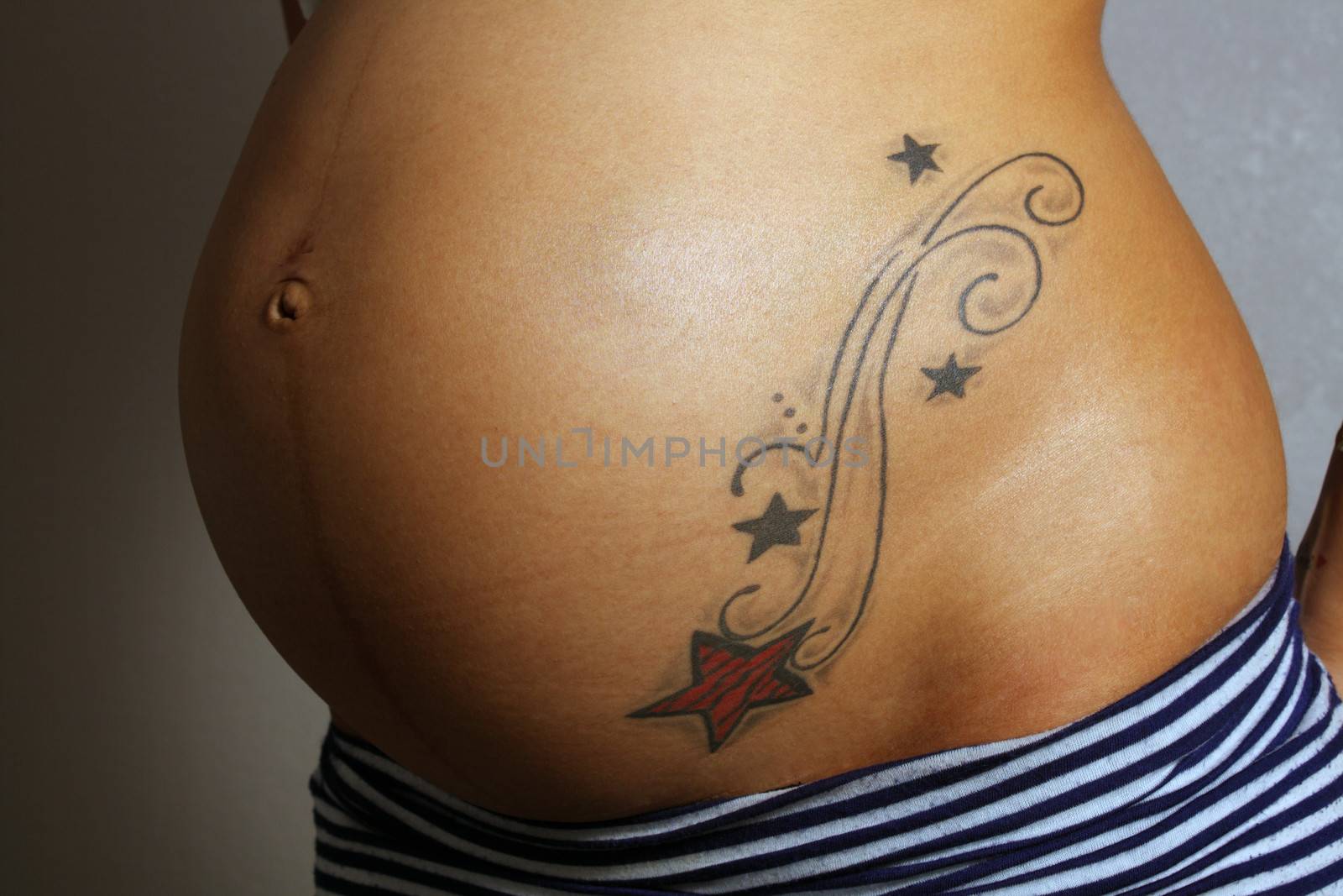 Close-up of the belly of an 8-month-pregnant woman with a tattoo.