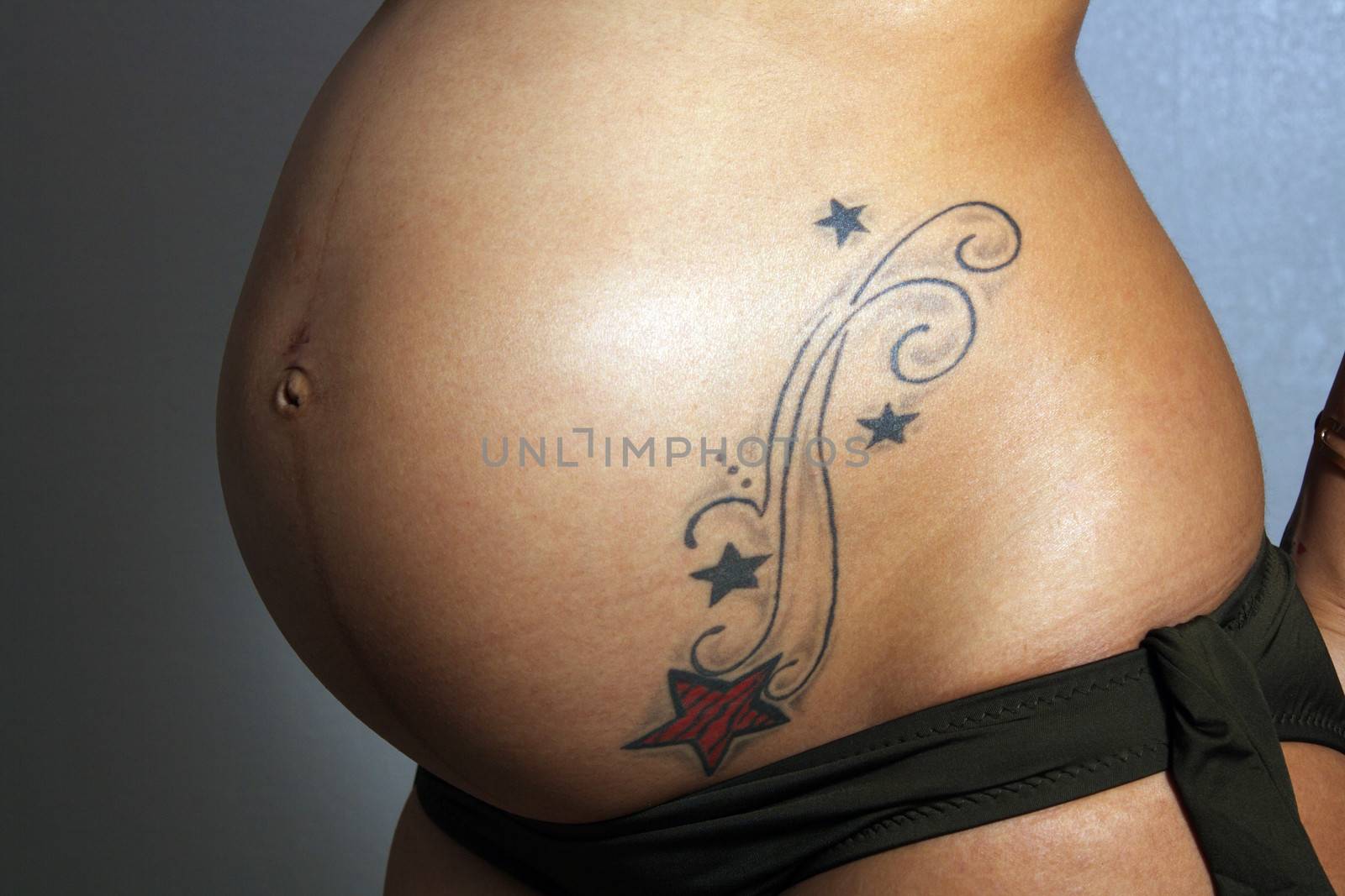 Close-up of the belly of an 8-month-pregnant woman with a tattoo.