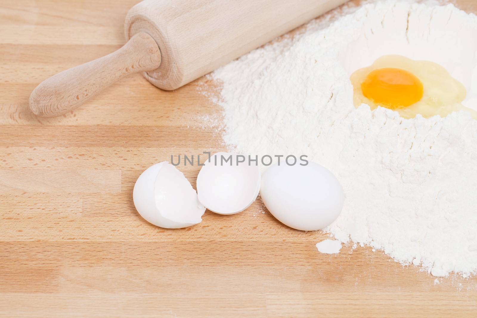 yolk in flour with a rolling pin from top with broken eggs on wooden background