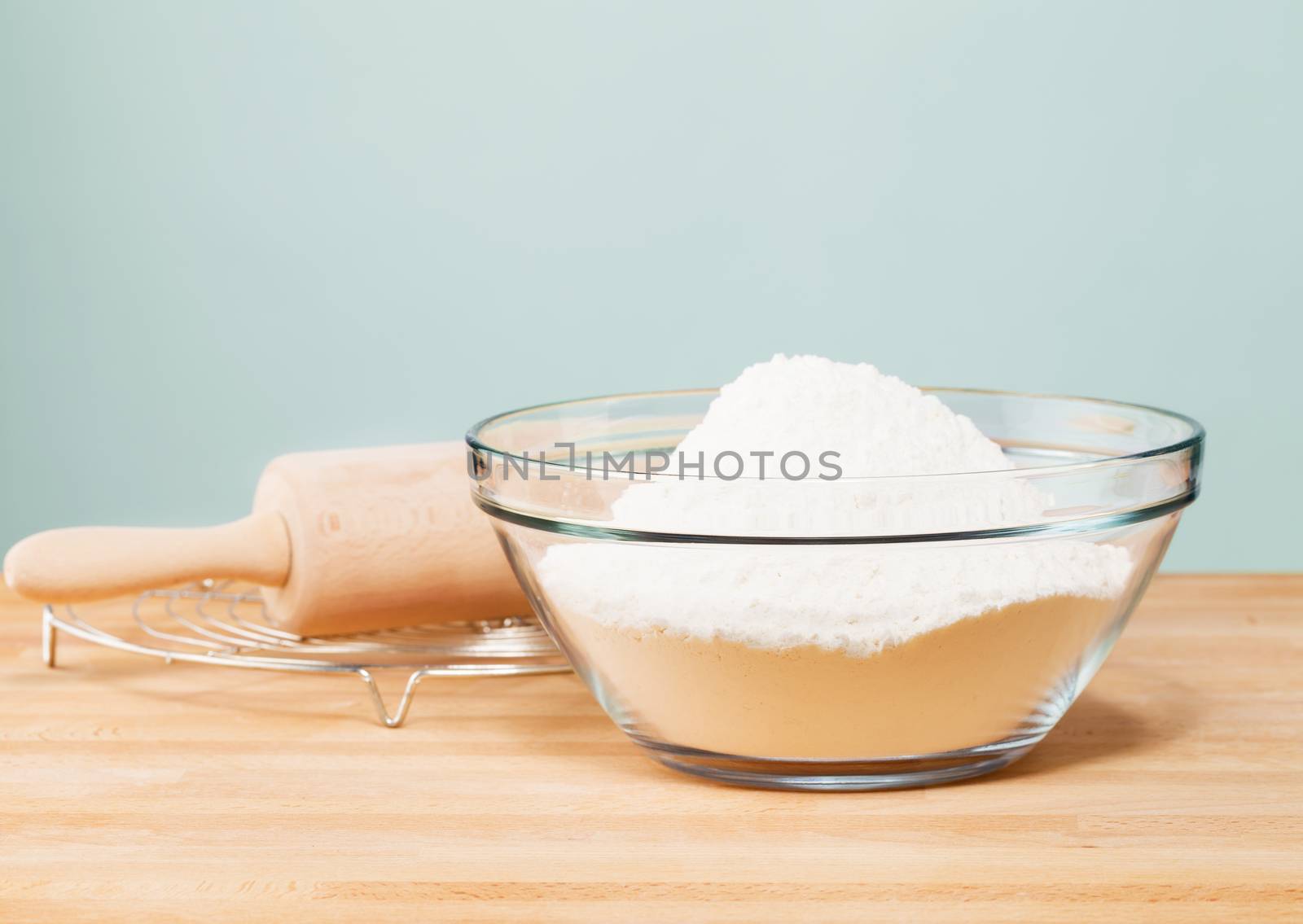 flour in a glass bowl with a rolling pin on with in front of a soft green wall