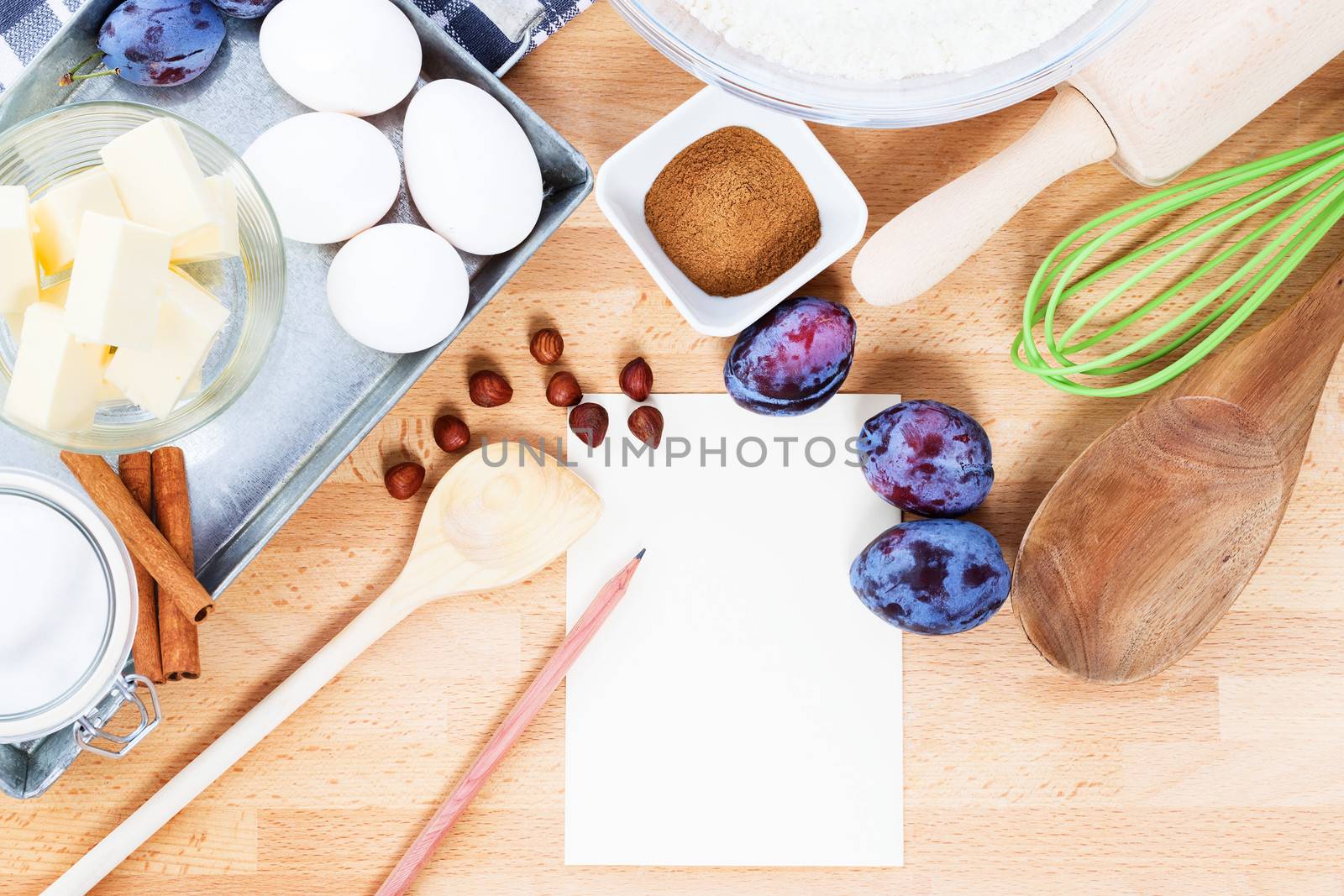 writing a recipe for plum cake with baking ingredients and tools from top with paper and a pencil