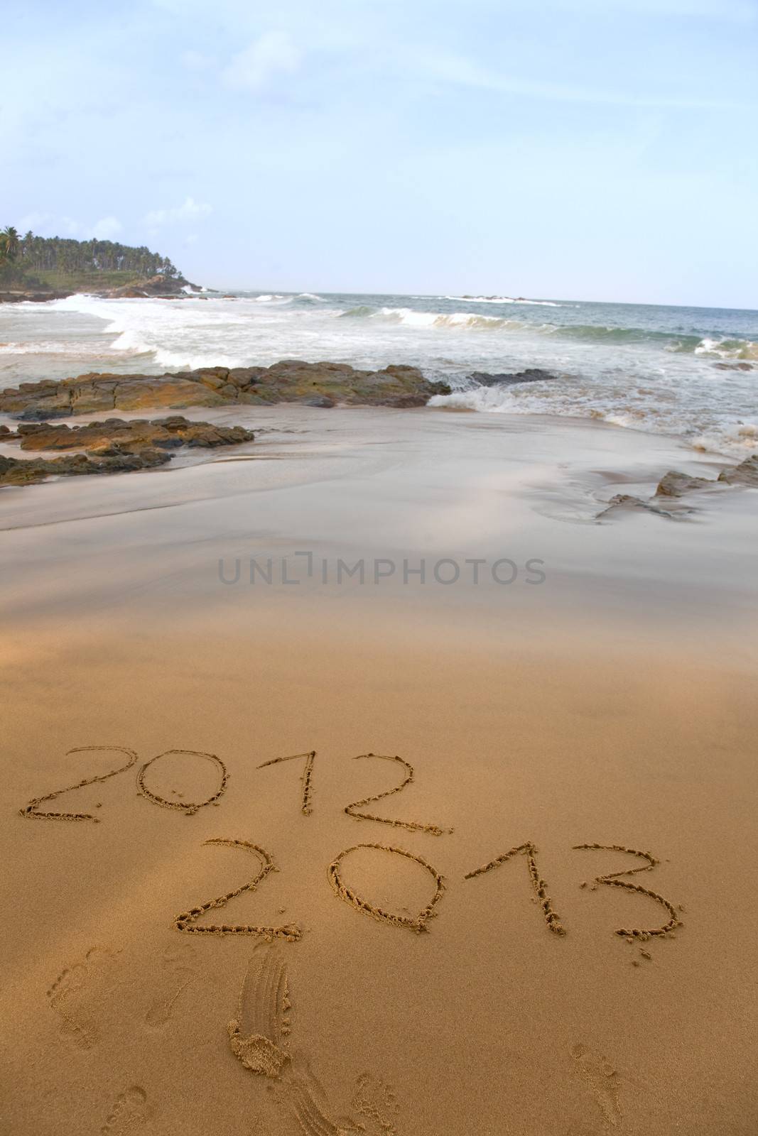 2012 and 2013 written in sand on beach with sea waves starting to erase the word 