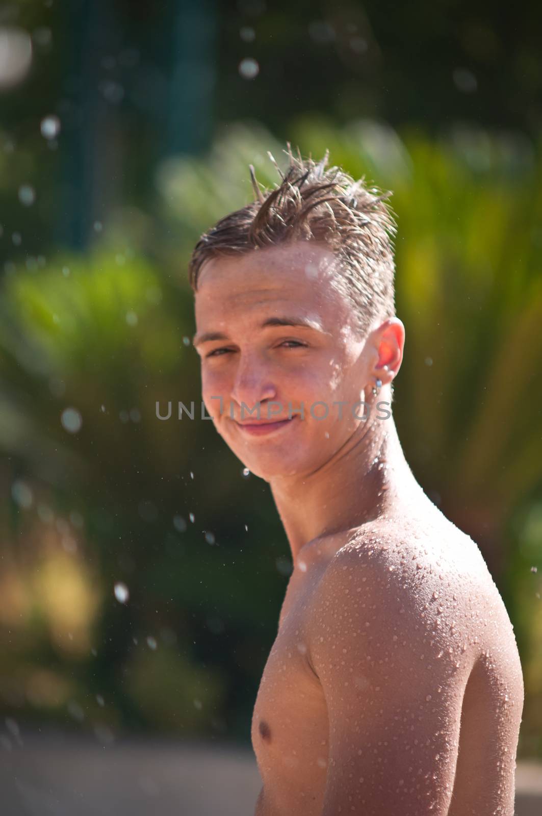 Wet teen in the spray of a fountain in a water park .