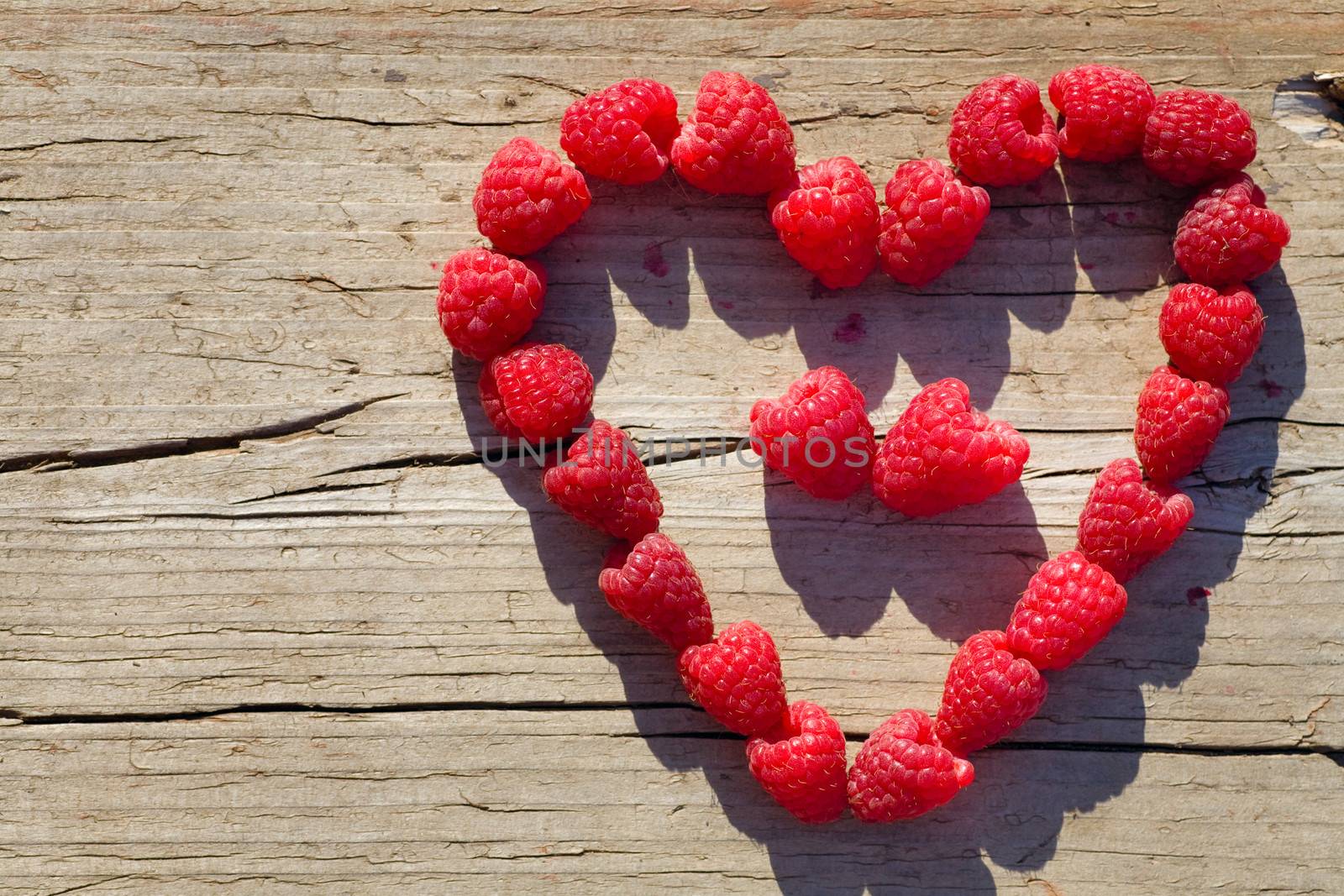 red Raspberry Heart  on wooden background in summer