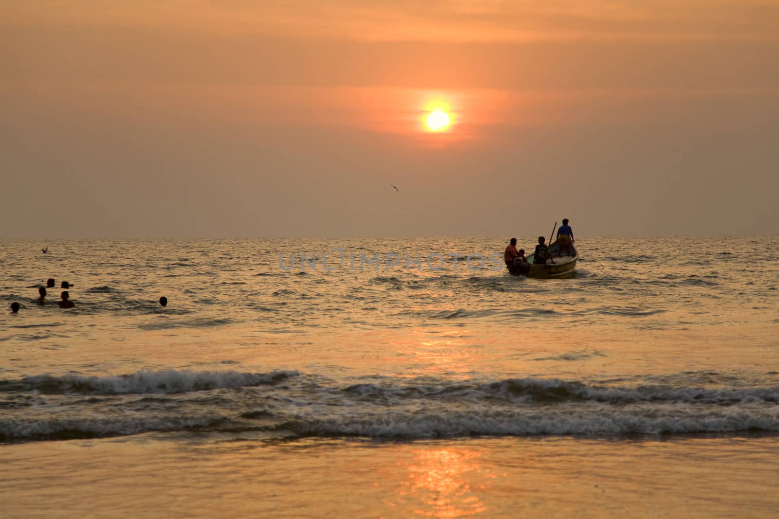 GOA, INDIA - 19 NOV 2011:  indian boat and swimming children at sunset in the seaon Arambol beach in Goa