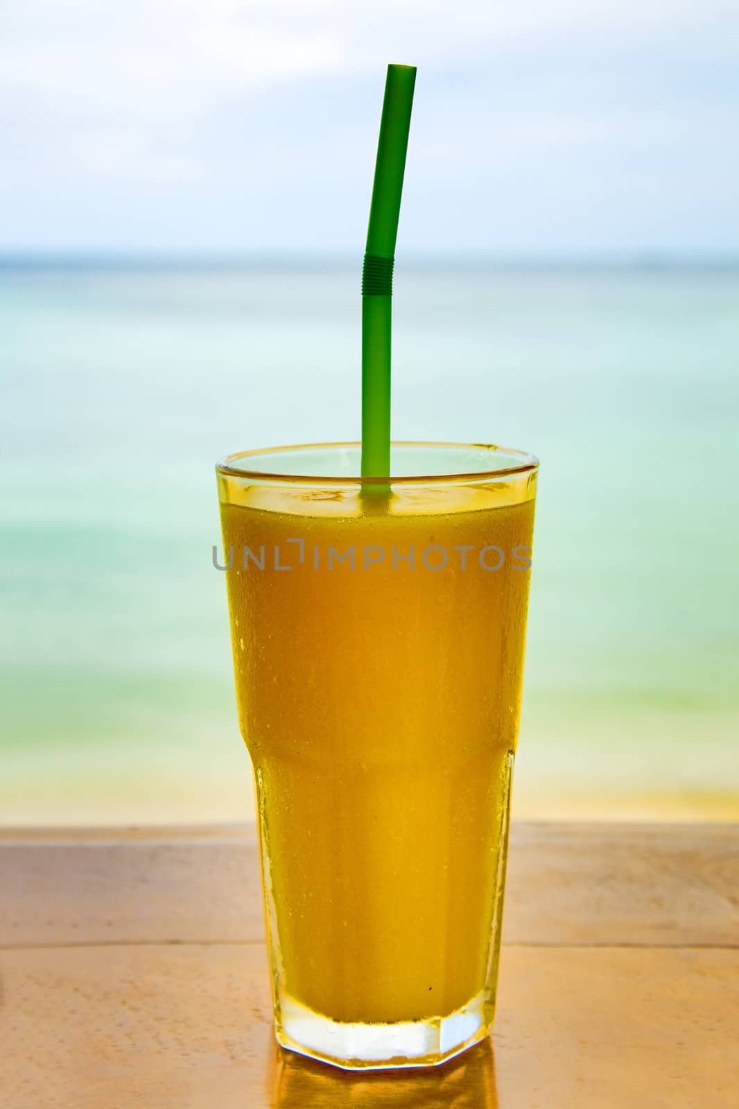 glass of  mango juice on the wooden table  against of the  sea