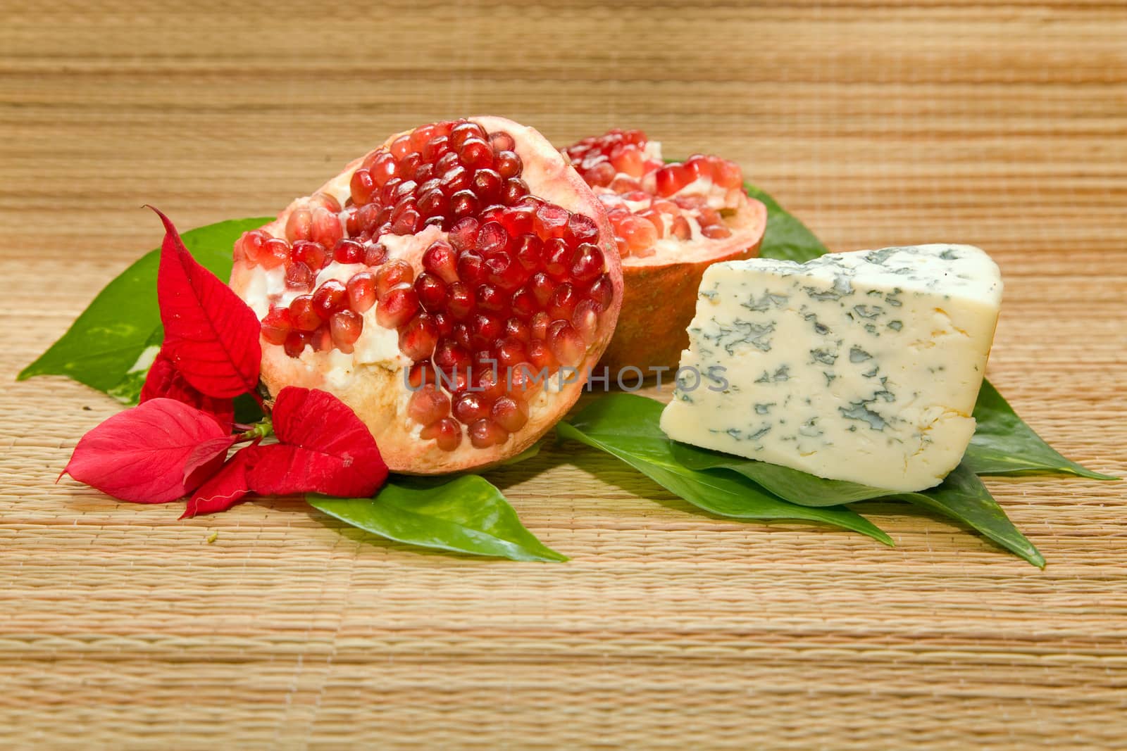 cheese with mold, pomegranate and leaf on matting