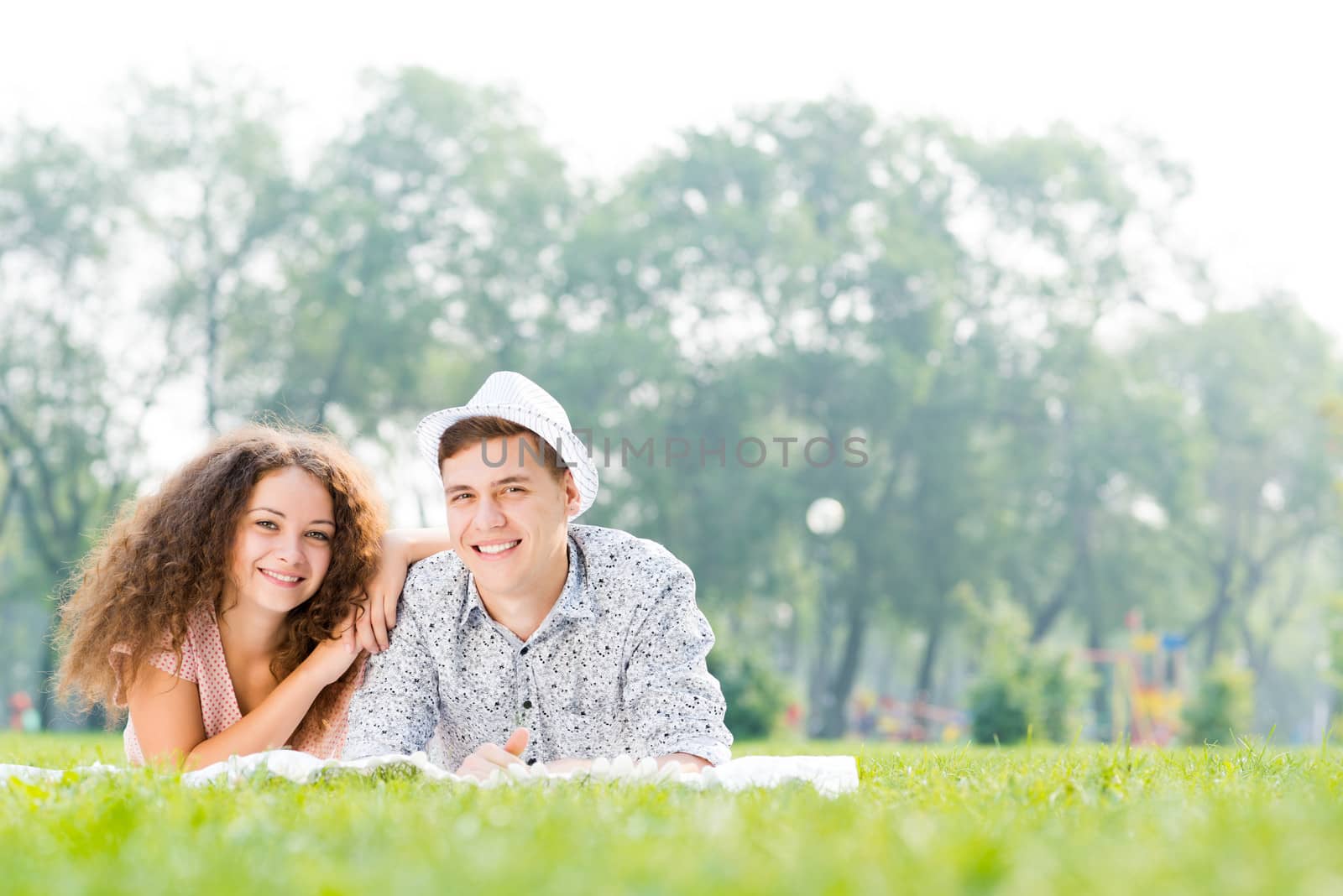 romantic couple lying on the grass in the summer park, spending time with loved ones