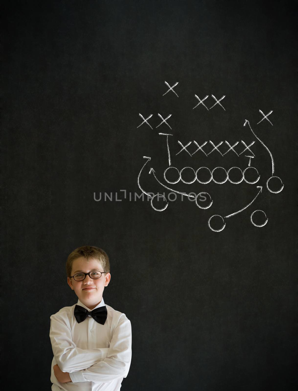 Thinking boy dressed up as business man with chalk American football strategy on blackboard background