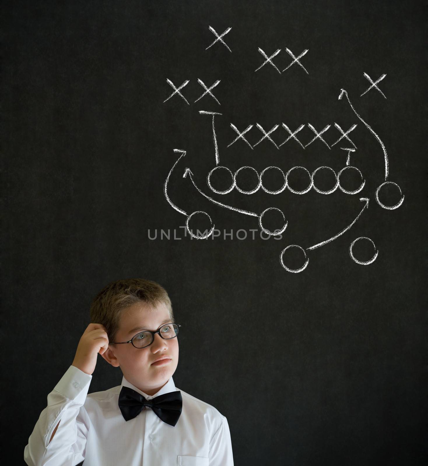 Scratching head thinking boy dressed up as business man with chalk American football strategy on blackboard background