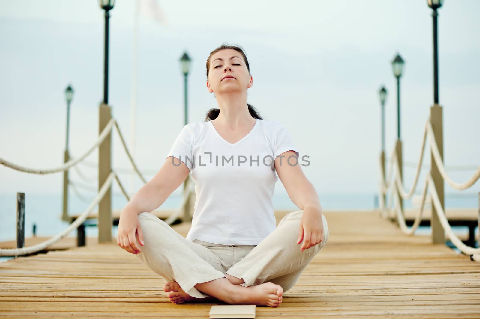 beautiful girl sitting in the lotus position on a pier with his eyes closed by kosmsos111