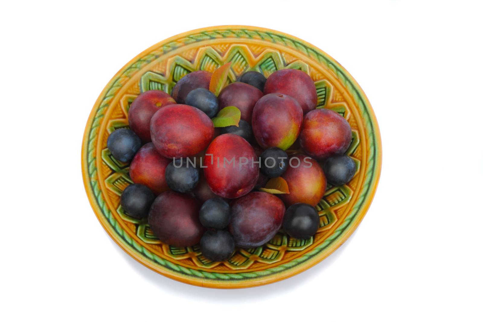 Large ripe purple plums and prunes in a ceramic dish . Presented on a white background.