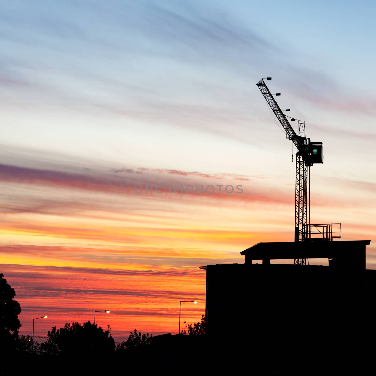 A construction crane silhouetted at sunset. (square frame)