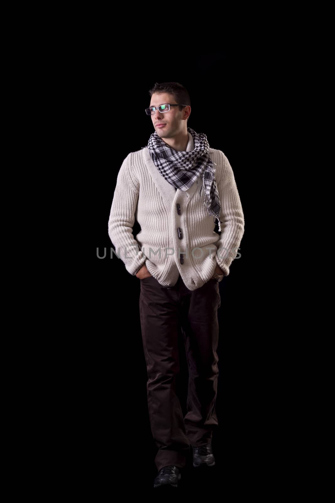 View of a young urban styled fashioned man walking isolated on a black background.