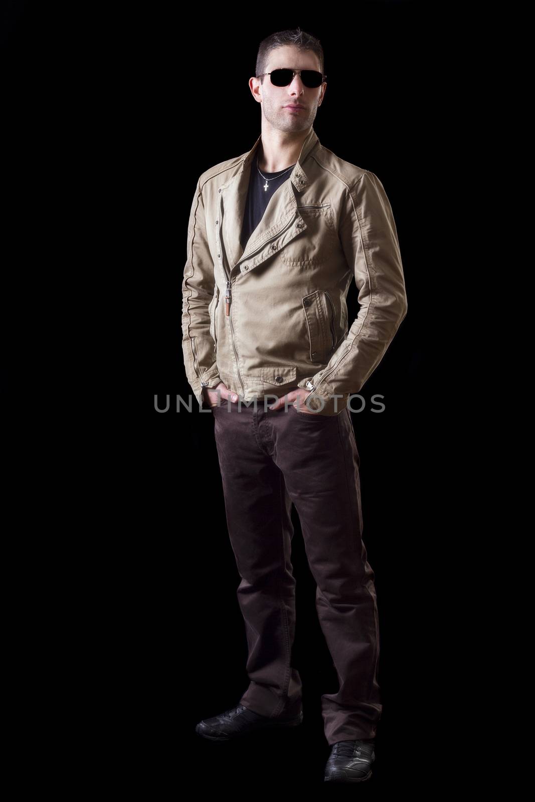 View of a young urban styled fashioned man standing isolated on a black background.