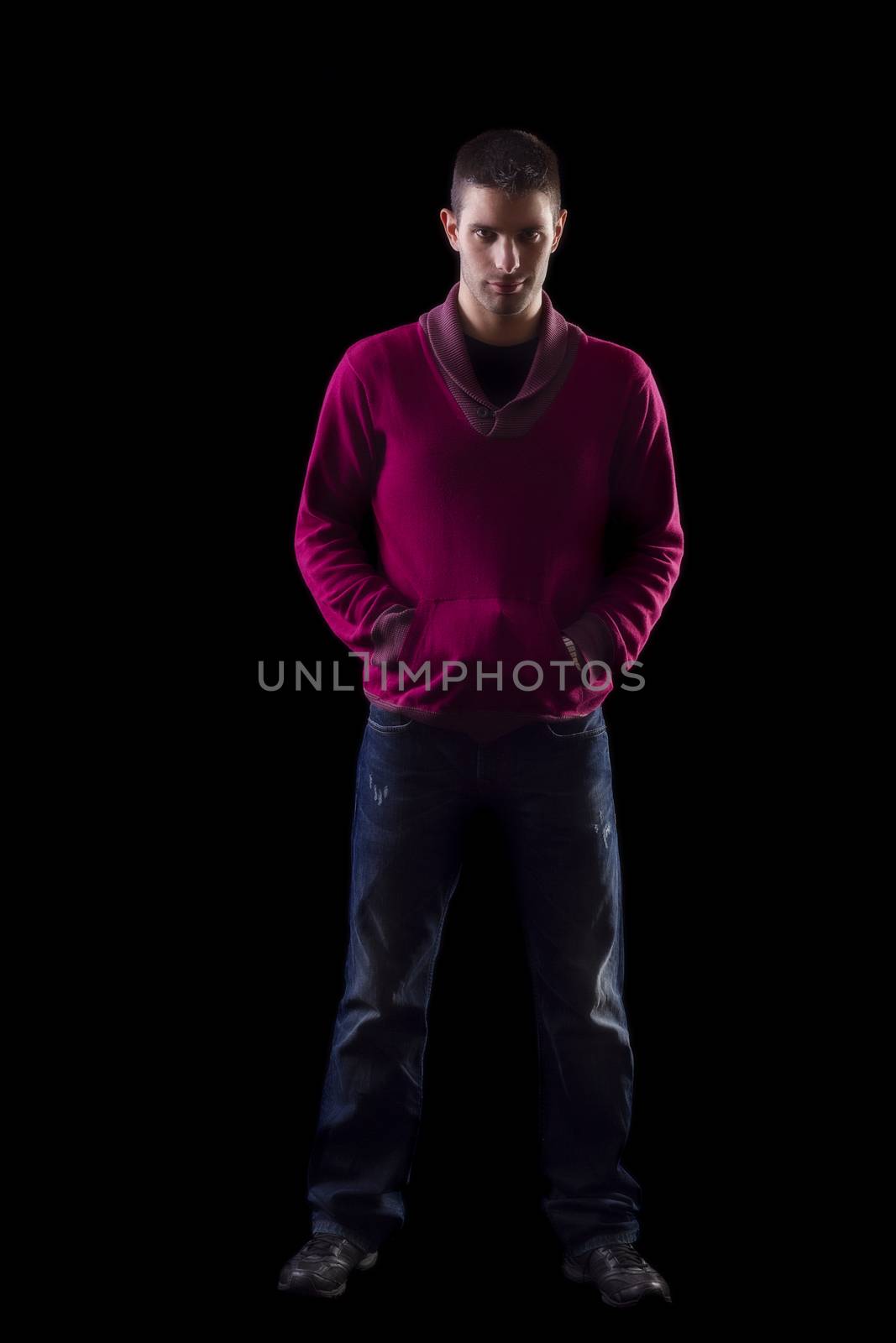View of a young urban styled fashioned man standing isolated on a black background.