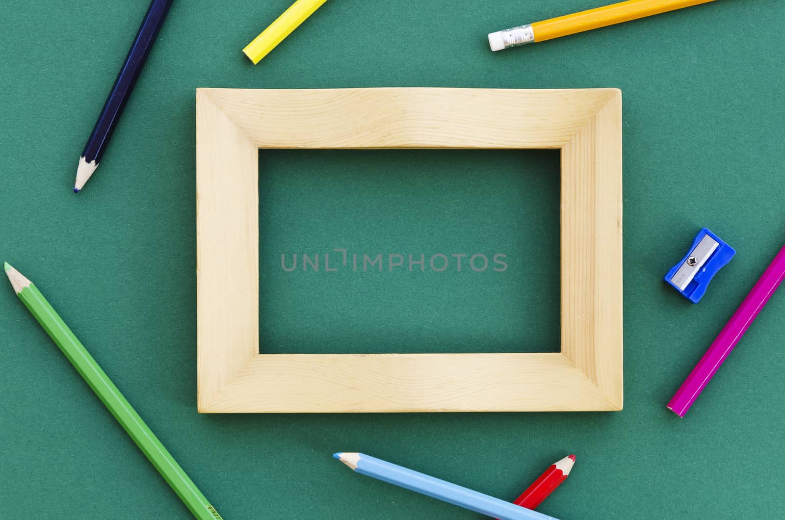 empty picture frame on a green background with pencil crayons and pencil sharpener