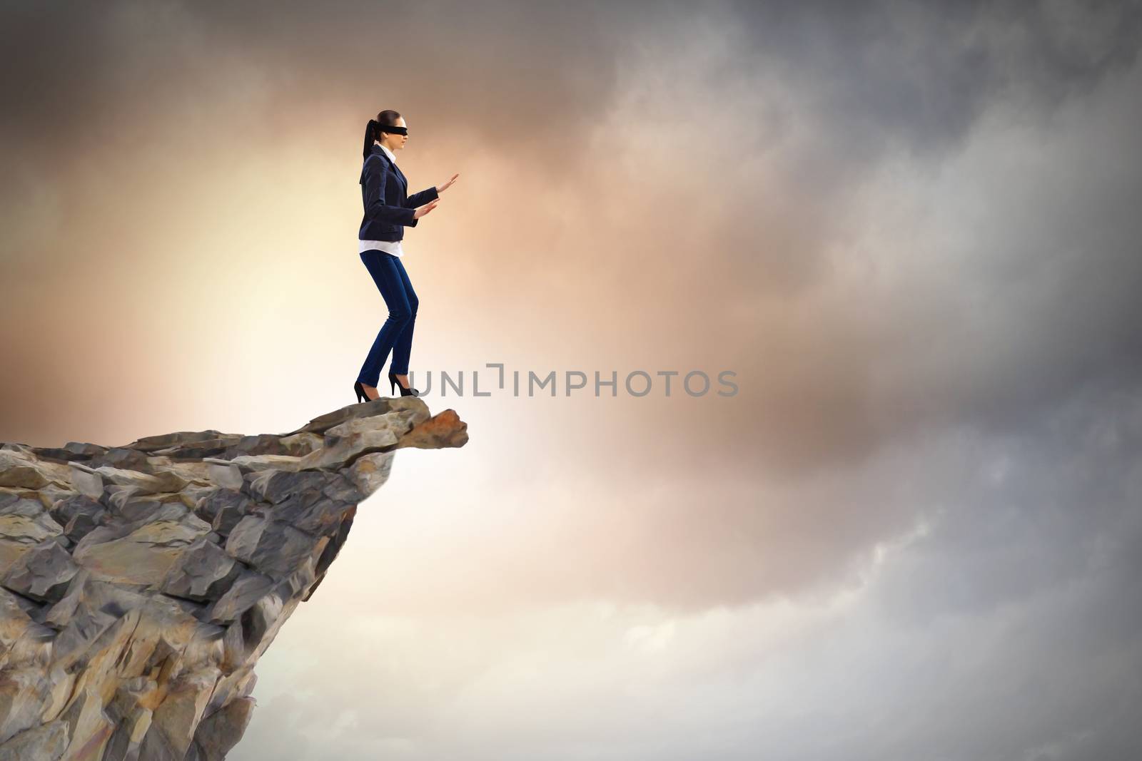 Image of businesswoman in blindfold standing on edge of mountain