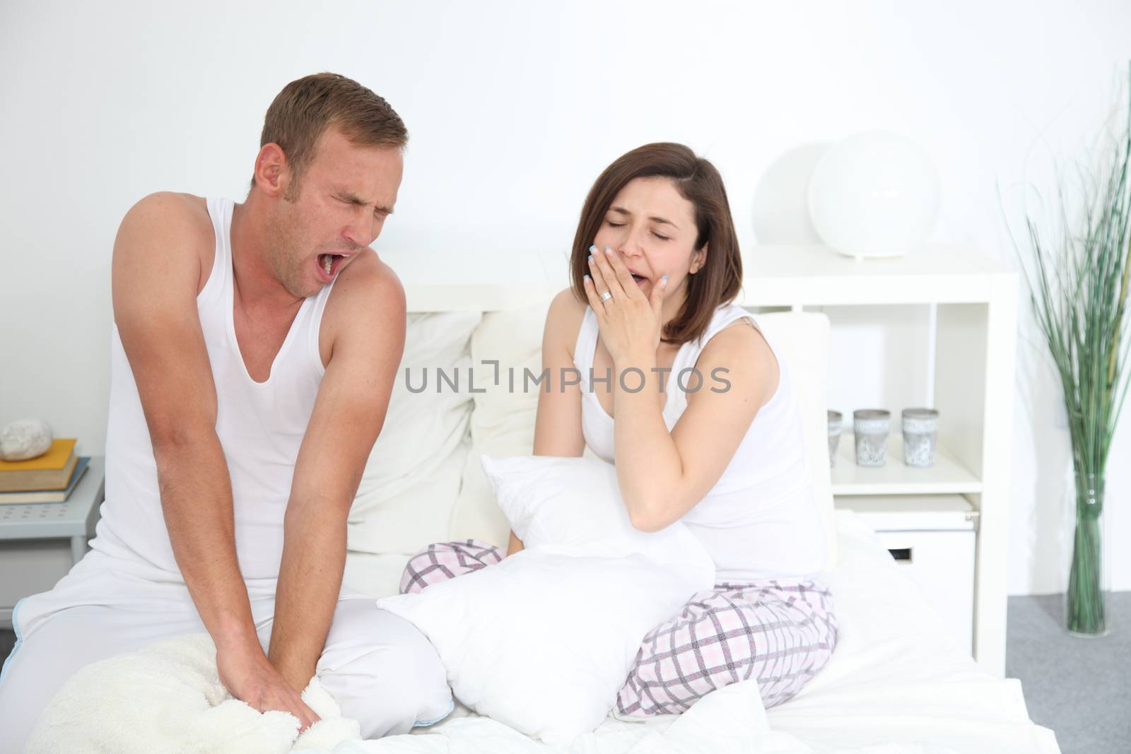 Middle-aged Caucasian sleepy couple yawning while sitting in bed in the bedroom