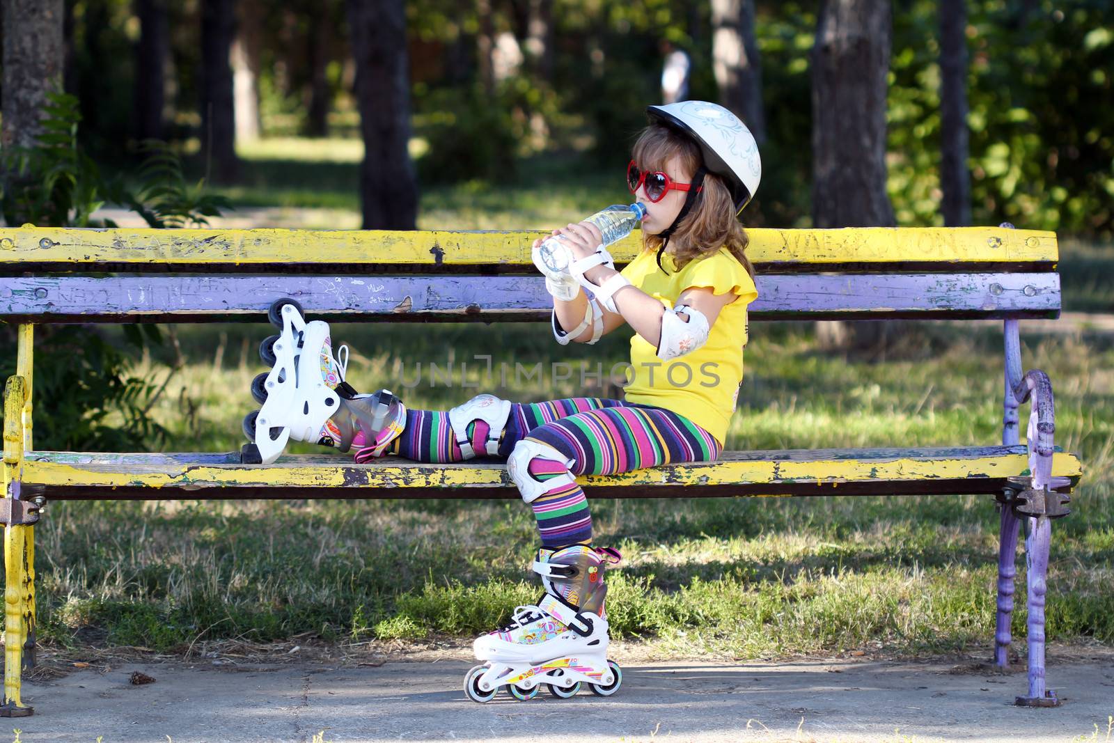 little girl with roller skates sitting on bench and drink water  by goce