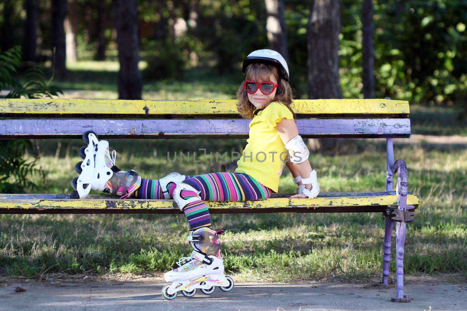 little girl with roller skates sitting on bench by goce