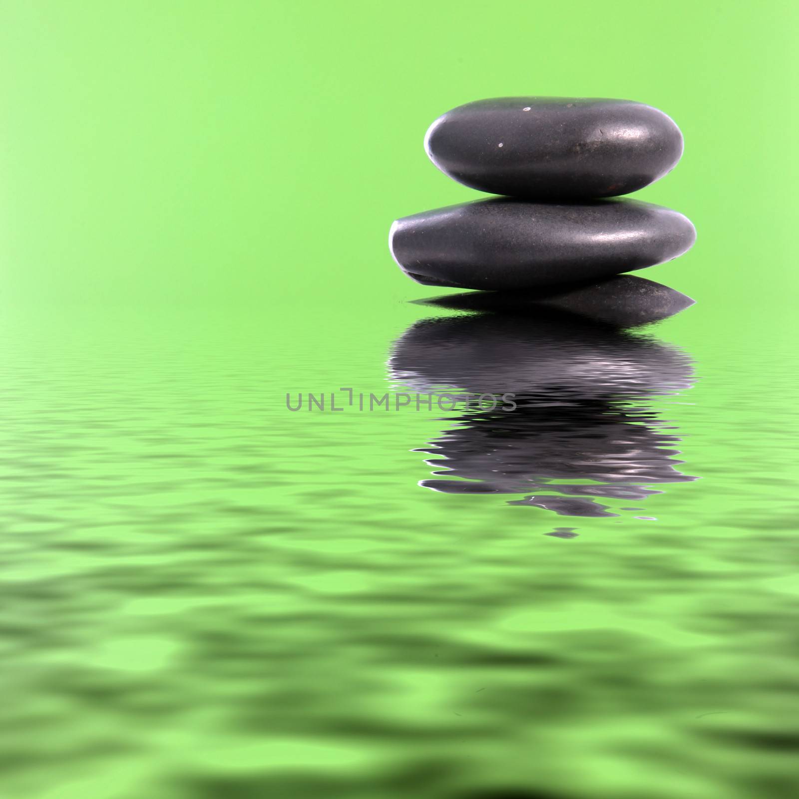 Fresh conceptual background with copyspace of a stack of smooth black basalt spa massage stones in green water with reflections