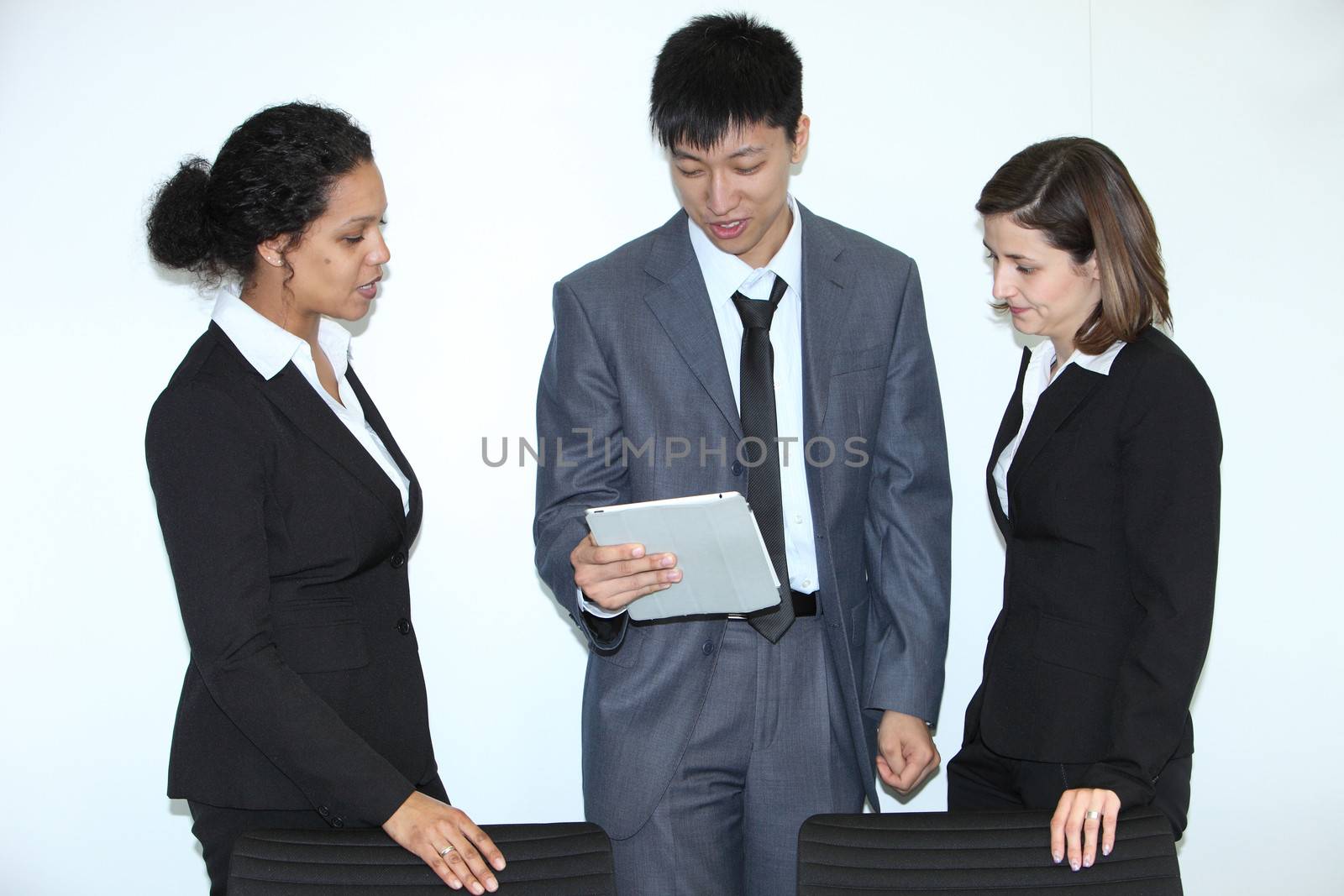 Multiethnic coworkers discussing a business problem standing together looking at a tablet held by a young Asian businessman