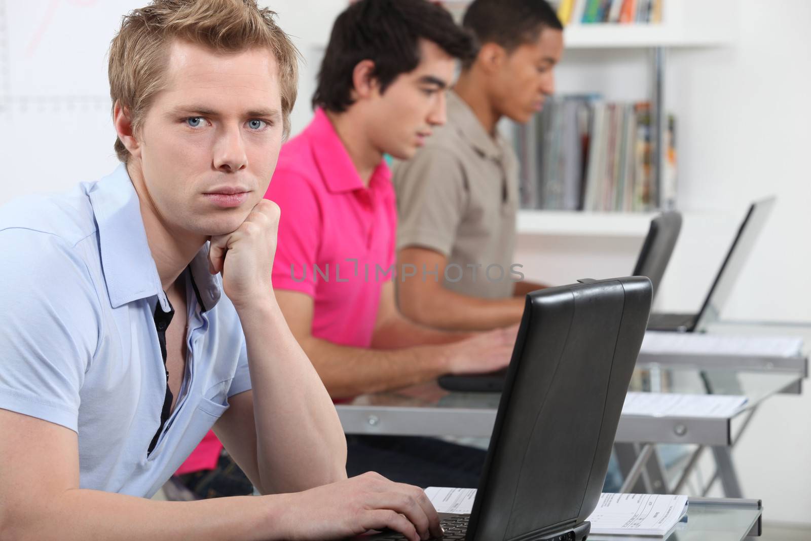 Three male students with laptops in classroom