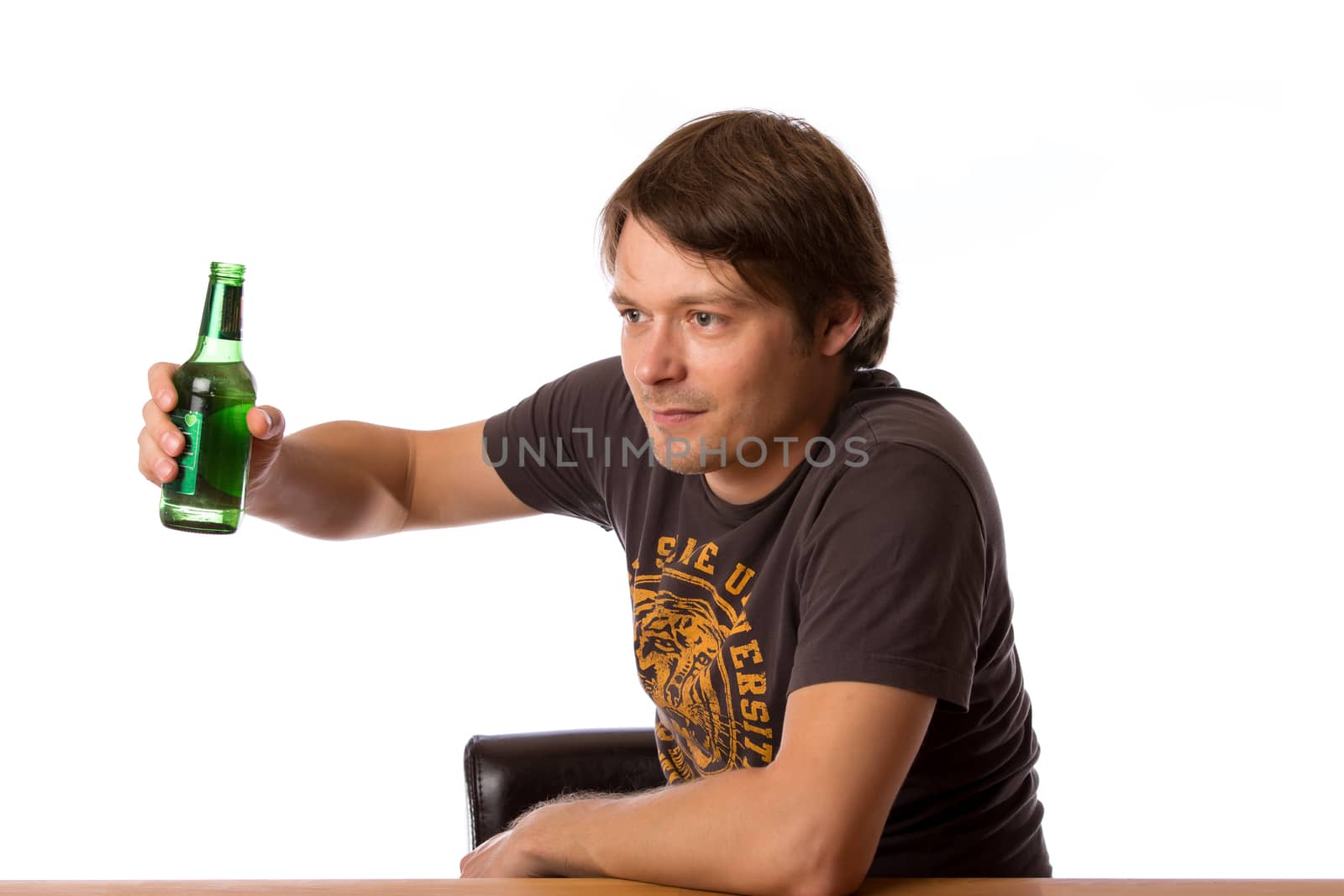 Man sitting at a wooden table with a bottle of beer.  Isolated on a white background