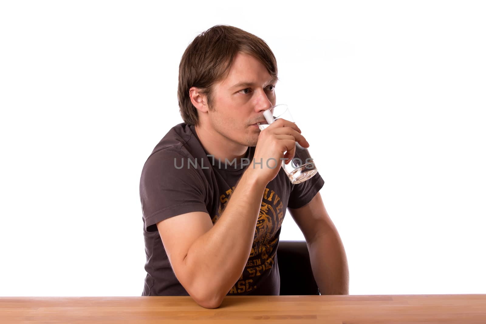 Man sitting at a wooden table and drinking water in a glass. Isolated on a white background