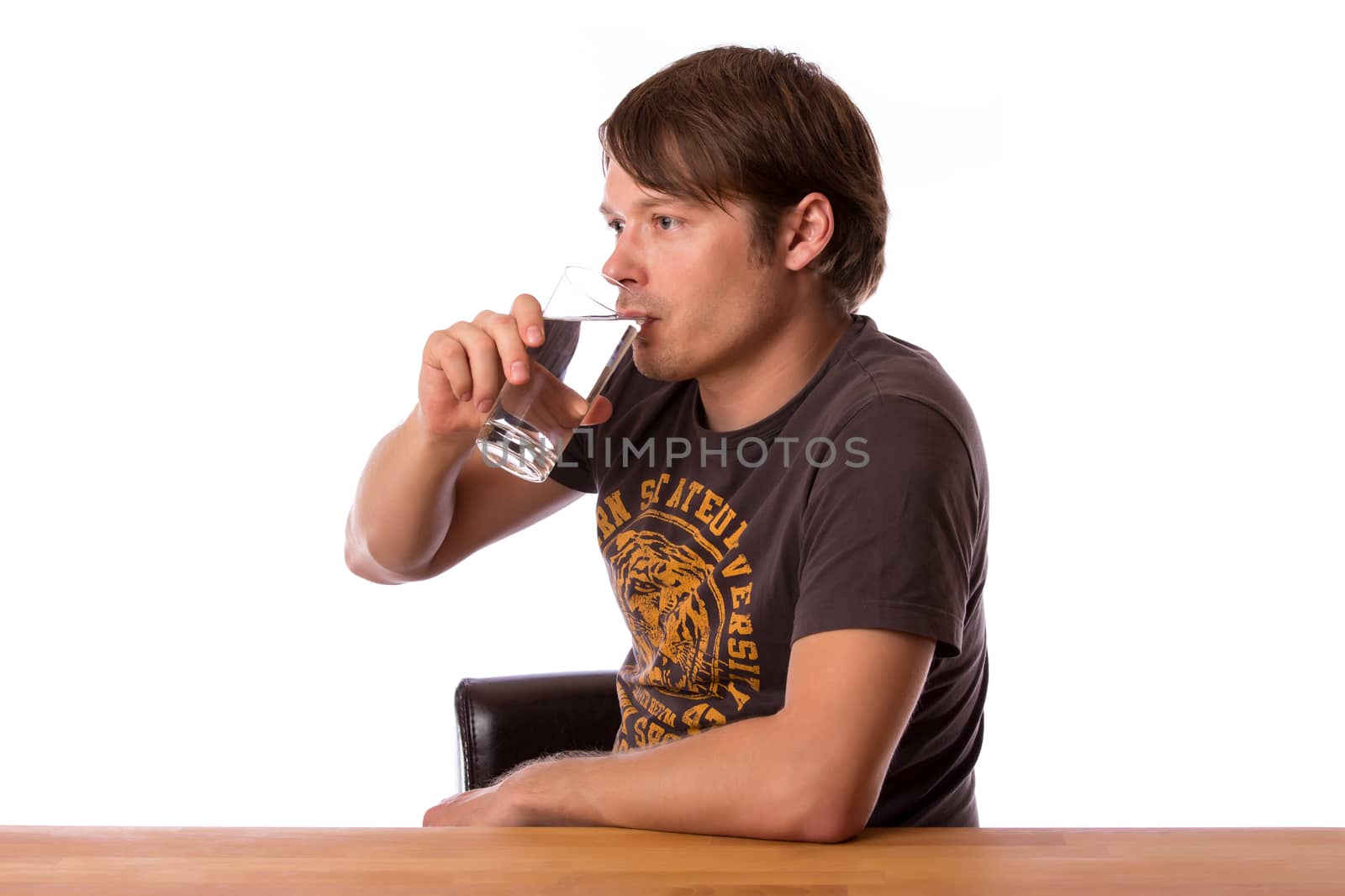 Man sitting at a wooden table and drinking water in a glass. Isolated on a white background