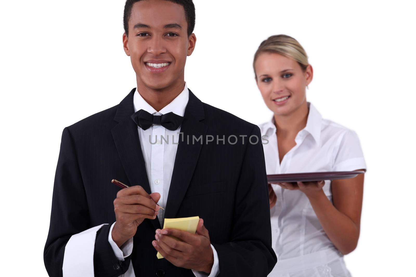 a young latino well dressed waiter writing order and a young blonde waitress holding a platter