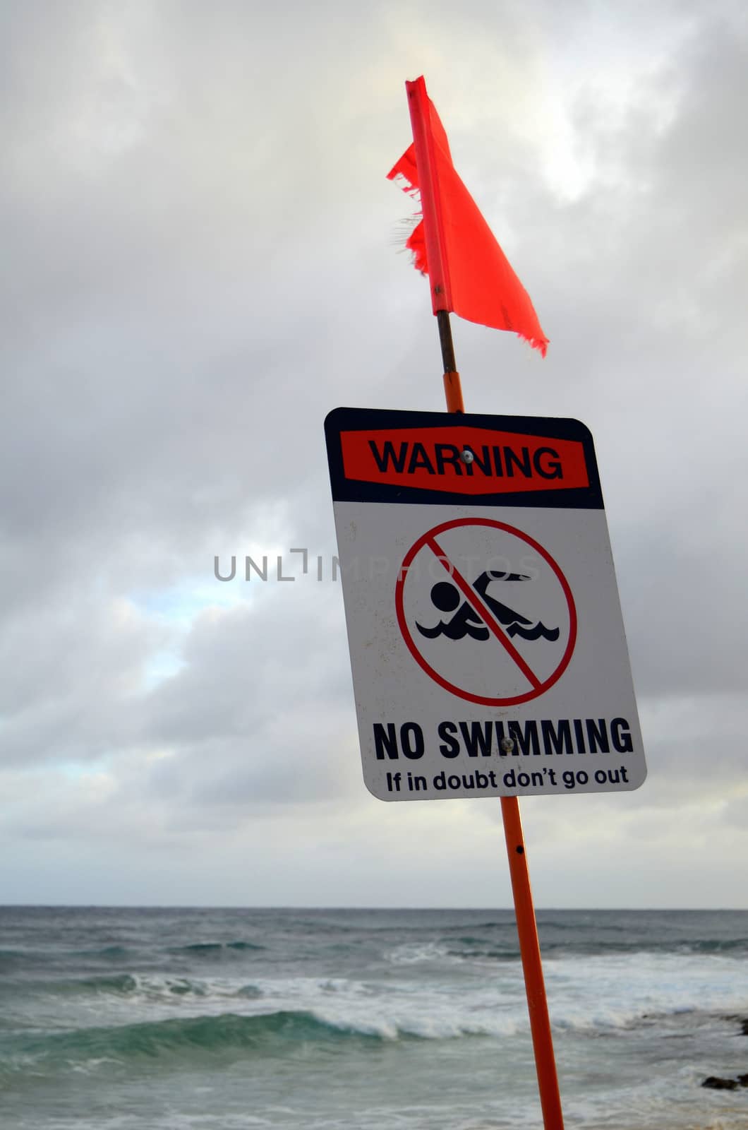 A no swimming warning sign beside a stormy beach