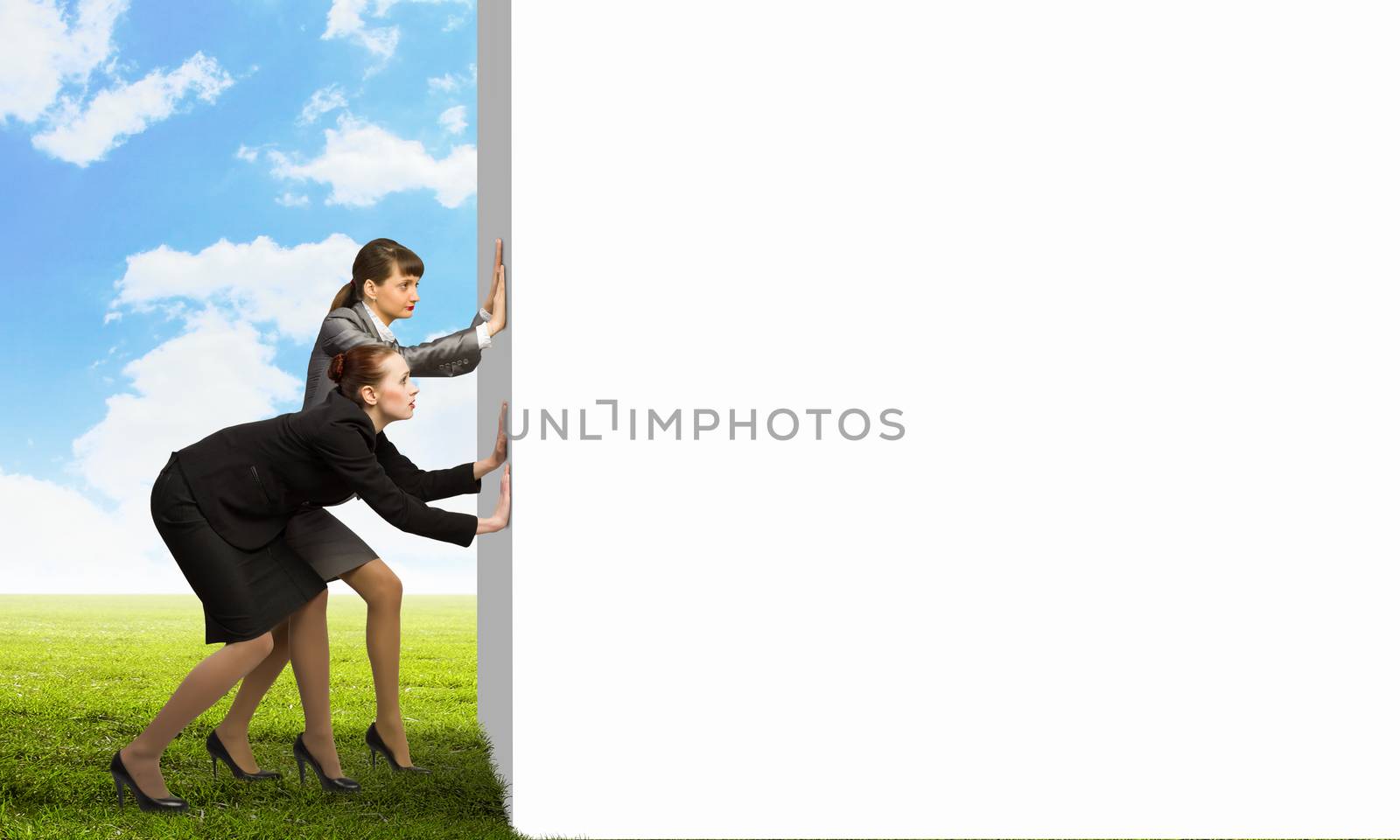 Image of two businesswomen pushing blank wall. Place for text