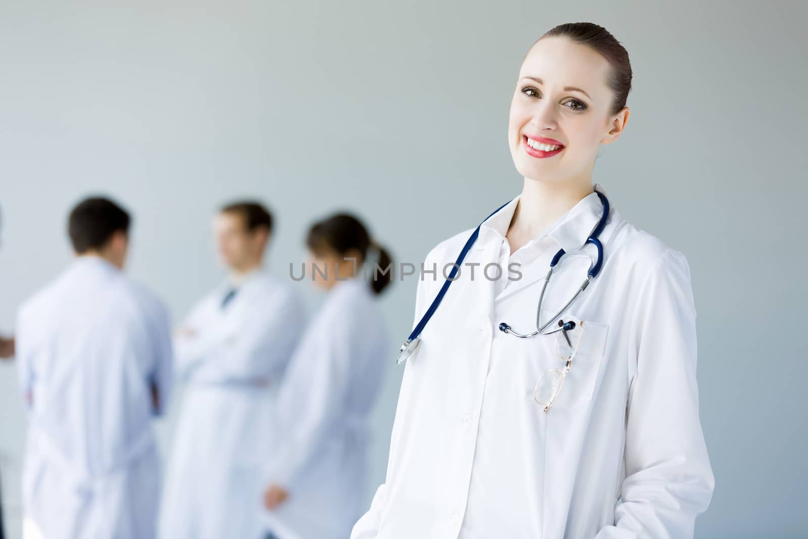 Attractive female doctor in white uniform with colleagues at background