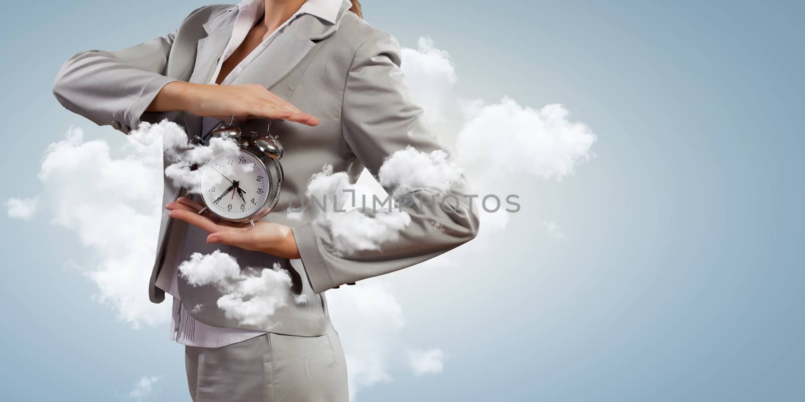 Image of young businesswoman holding alarmclock against cloudy background