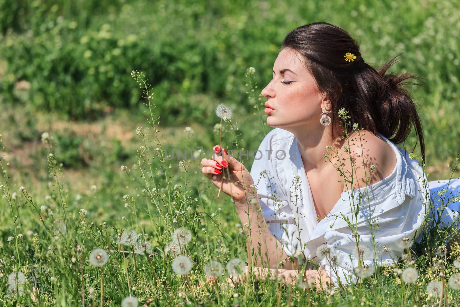Girl with dandelion lying on green grass