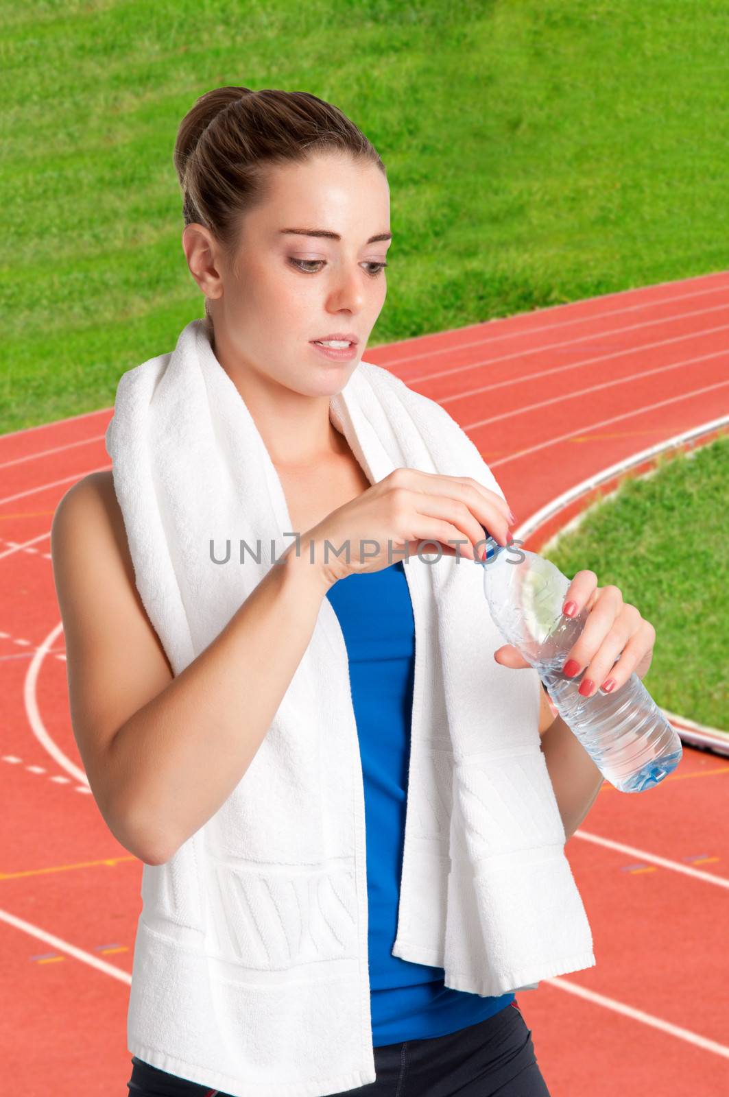 Woman about to drink water from a plastic bottle, with a running track behind her