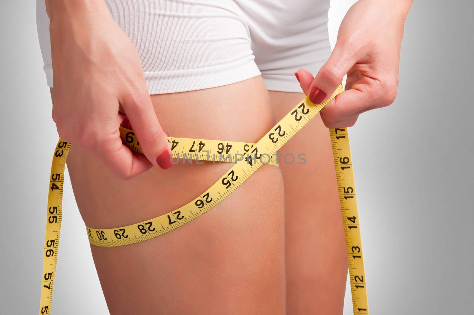 Woman measuring her thigh with a yellow measuring tape