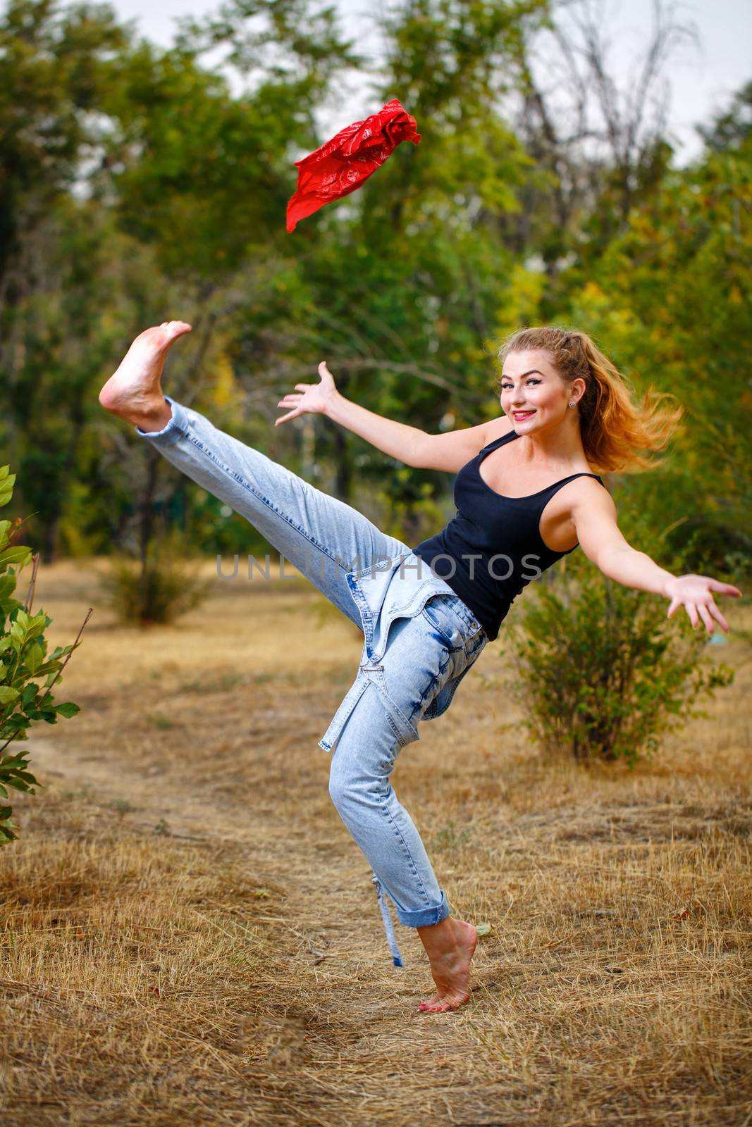 Beautiful pin-up girl barefoot in jeans overalls throws a red bandanna