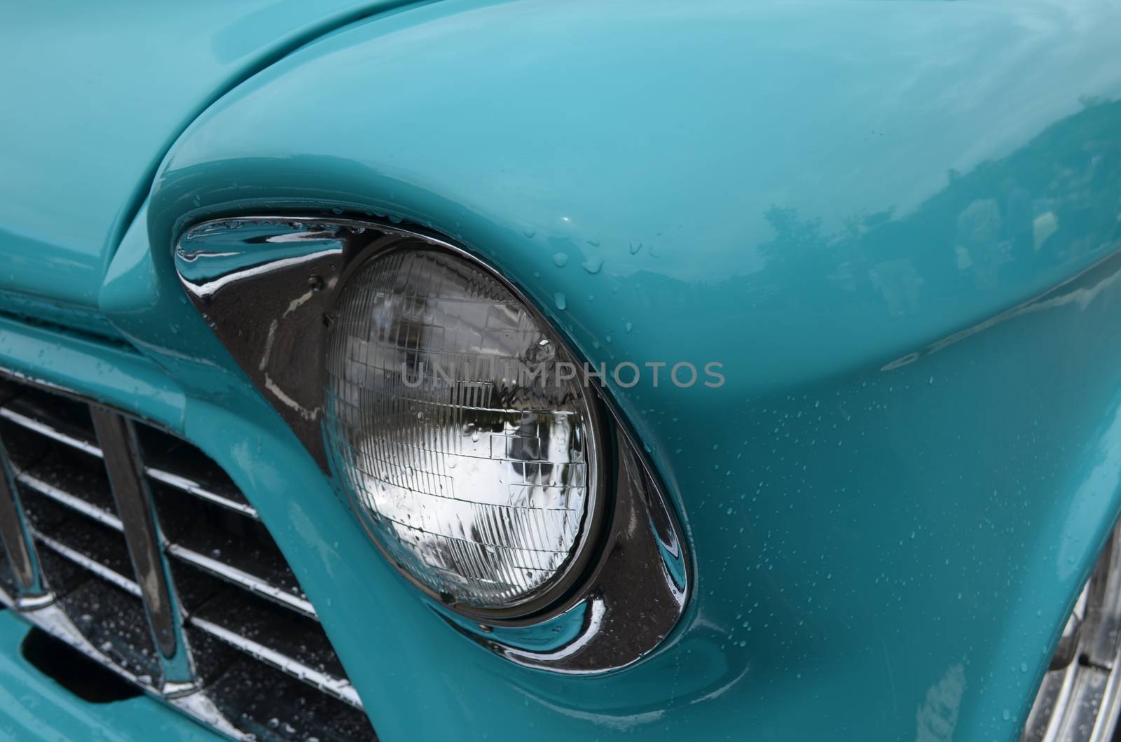 Beautiful restored American classic car with its headlamp and chrome surround shining with rain drops on its paint work.