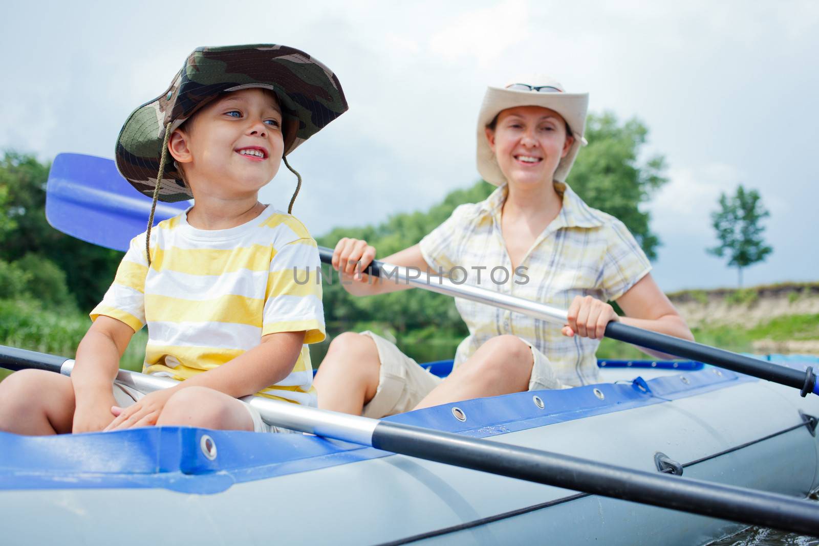 Happy young boy with mother paddling kayak on the river in lovely summer day