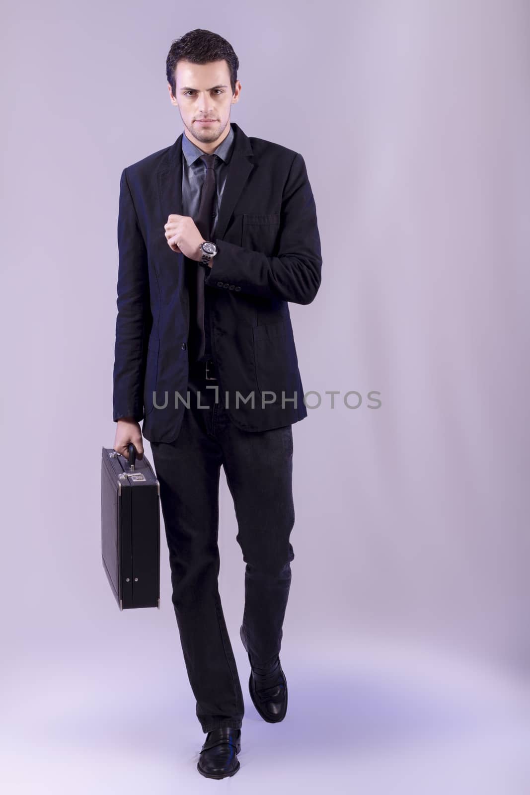 View of a young business man walking against a grey  background. 